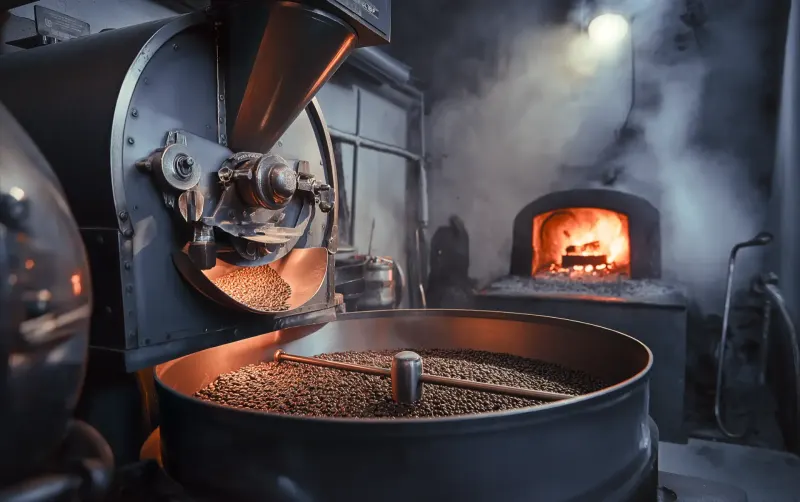 Roasting machine with freshly roasted coffee beans, a burning wood stove in the background